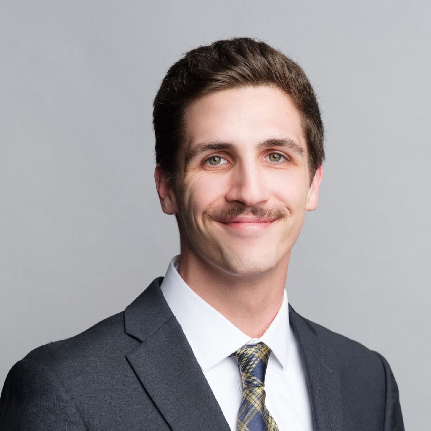 Man in suit with mustache, smiling confidently.
